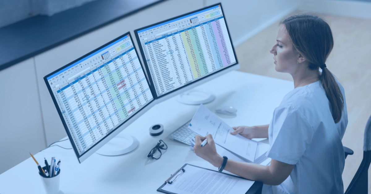 Woman sits in front of dual monitors with spreadsheets open