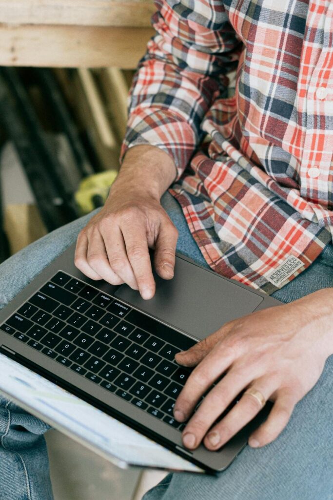 Craftsman working on laptop in woodworking workshop, surrounded by tools.